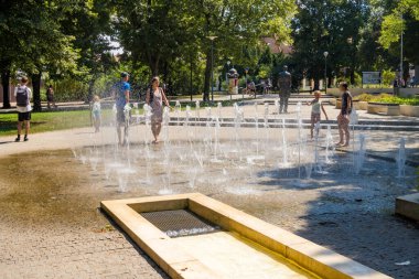 Podebradi- Çek- 27 Temmuz 2024: İnsanlar ağaçların gölgesindeki sıcaktan ve su damlalarından, Central Park 'taki çeşmeden kaçıyorlar. Yüksek kalite fotoğraf