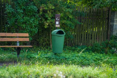 Parkta çöp tenekesi olan modern bir ahşap bank. Köpekler için poşetleri olan çöp tenekesi. Dinlenme alanında rahat bir bank. Şehir gelişimi, şehir planlaması, kamusal alanlar. Yüksek kalite fotoğraf
