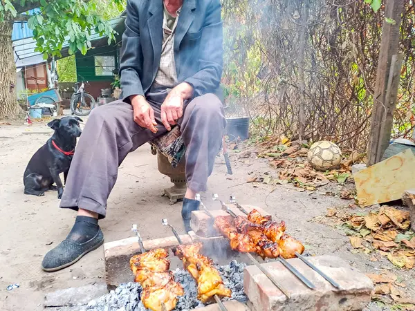 Köpeği olan yaşlı bir adam Ukrayna 'da bir şenlik ateşinde avlusunda et kızartıyor. Elektrik kesintisi. Yüksek kalite fotoğraf