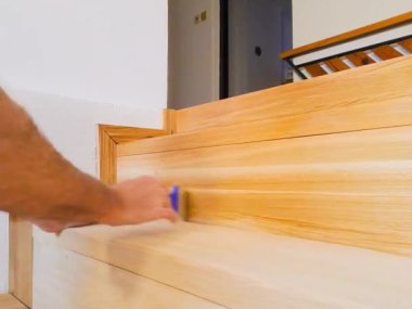 Yeni merdiven cilası süren bir adamın yakın çekimi. Tahta tasarımı. Tahtaların yağlı kaplamaları. Yeni katman. İnşaat işi. Matte ve parlak yüzey. Doğal ahşap malzemeler. Yüksek kaliteli HD görüntüler