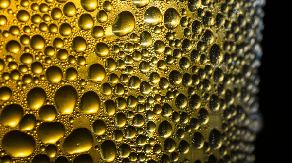Close-up of water droplets from a glass of cold beer condensing, on a golden yellow background