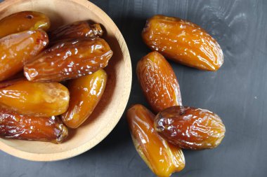 Kurma meyveleri, siyah arka planda küçük tahta kaselerde.