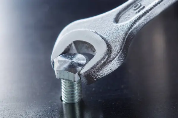 Wrench tightens bolt in steel billet. Spanner, bolt, screw and nuts.