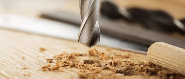 drill bit makes hole in wooden oak board for wooden dowel.