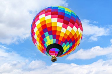 Mavi gökyüzünde beyaz bulutlarla uçan renkli sıcak hava balonu
