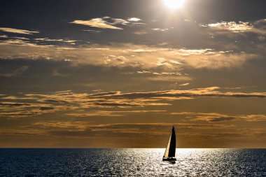 Gün batımında, Artruxt Deniz feneri, Cuidadela, Menorca, Balear Adaları 'nın önünden geçen bir yelkenli teknesinin görüntüsü.