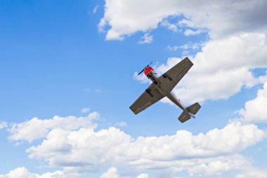 Aerobatik bir uçak (aerodyne), beyaz bulutlu mavi bir gökyüzünün altında uçarken görülüyor. uçuş sergileri