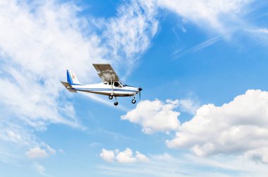 Tek motorlu ultrallight uçak, mavi gökyüzünde beyaz bulutlarla uçuyor.