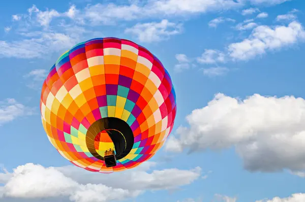 Mavi gökyüzünde beyaz bulutlarla uçan renkli sıcak hava balonu
