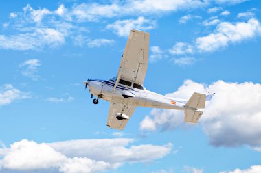 Tek motorlu ultrallight uçak, mavi gökyüzünde beyaz bulutlarla uçuyor.