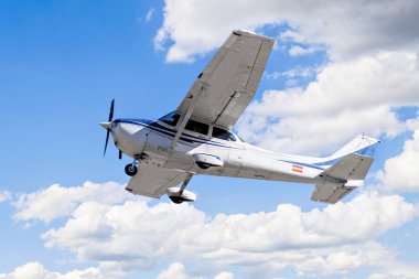 Tek motorlu ultrallight uçak, mavi gökyüzünde beyaz bulutlarla uçuyor.