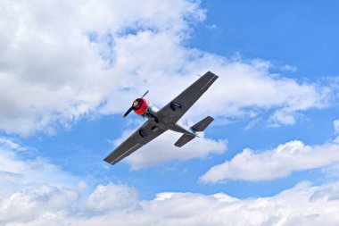 Aerobatik bir uçak (aerodyne), beyaz bulutlu mavi bir gökyüzünün altında uçarken görülüyor. uçuş sergileri