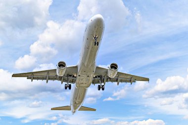 Airbus A321 yolcu uçağı beyaz bulutlu mavi gökyüzünün altında havaalanına iniyor.