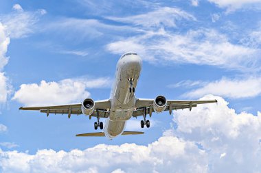 Airbus A321 yolcu uçağı beyaz bulutlu mavi gökyüzünün altında havaalanına iniyor.