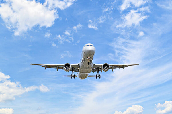 Пассажирский самолет приземляется в аэропорту, под голубым небом с белыми облаками
