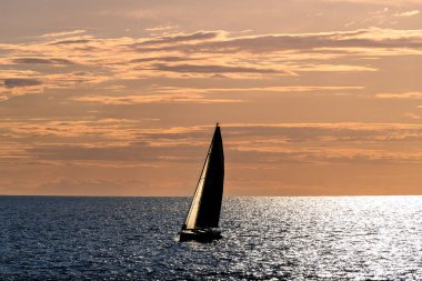 Gün batımında, Artruxt Deniz feneri, Cuidadela, Menorca, Balear Adaları 'nın önünden geçen bir yelkenli teknesinin görüntüsü.