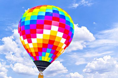Mavi gökyüzünde beyaz bulutlarla uçan renkli sıcak hava balonu