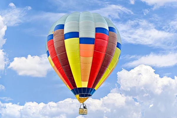 Mavi gökyüzünde beyaz bulutlarla uçan renkli sıcak hava balonu