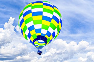 Mavi gökyüzünde beyaz bulutlarla uçan renkli sıcak hava balonu