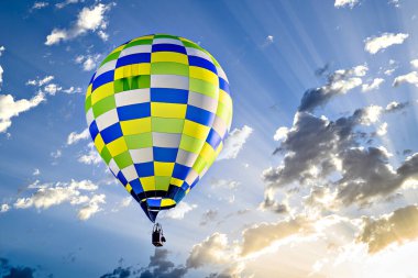 Mavi gökyüzünde beyaz bulutlarla uçan renkli sıcak hava balonu