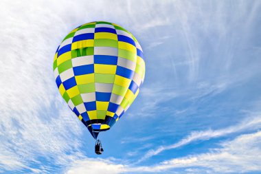 Mavi gökyüzünde beyaz bulutlarla uçan renkli sıcak hava balonu