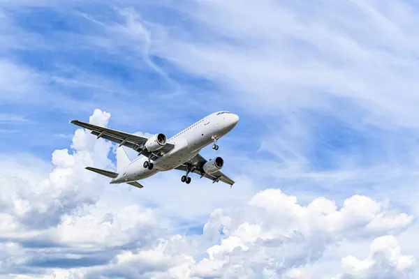 Yolcu uçağı beyaz bulutlu mavi gökyüzünün altında havaalanına iniyor.