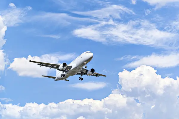 Yolcu uçağı beyaz bulutlu mavi gökyüzünün altında havaalanına iniyor.