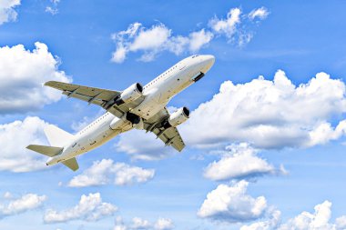 Yolcu uçağı beyaz bulutlu mavi gökyüzünün altında havaalanına iniyor.