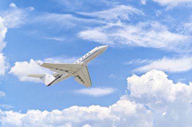 Mavi gökyüzünün altında beyaz bulutlarla uçan özel bir iş uçağı.