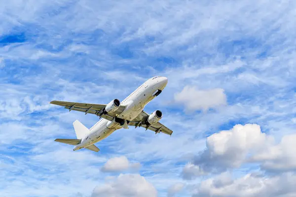 Yolcu uçağı beyaz bulutlu mavi gökyüzünün altında havaalanına iniyor.