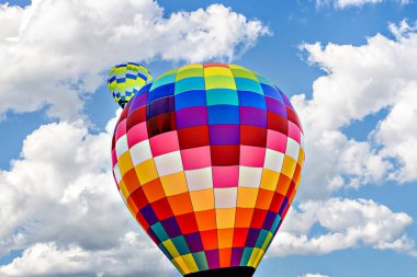 Mavi gökyüzünde beyaz bulutlarla uçan renkli sıcak hava balonu