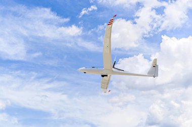 Mavi gökyüzünde beyaz bulutlarla uçan tek motorlu ultra hafif uçak.