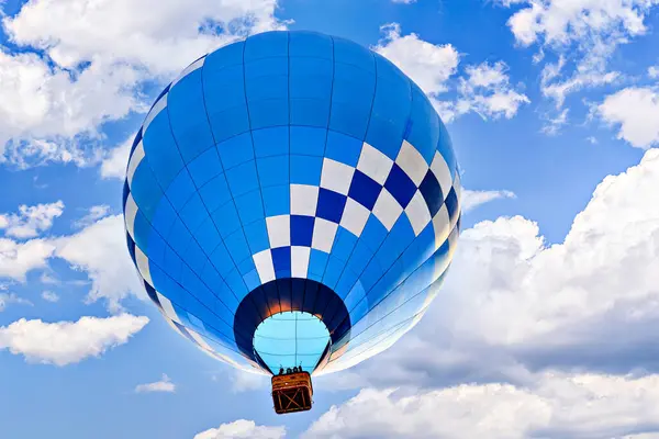 Mavi sıcak hava balonu mavi gökyüzünde beyaz bulutlarla uçuyor.
