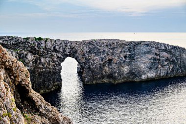 Ciutadella, Menorca, Balearic Adaları 'ndaki Pont den Gil Cala Corbetar' da muhteşem bir günbatımı. Kemer şeklinde tuhaf bir doğal oluşum.