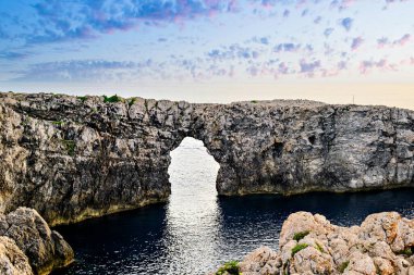 Ciutadella, Menorca, Balearic Adaları 'ndaki Pont den Gil Cala Corbetar' da muhteşem bir günbatımı. Kemer şeklinde tuhaf bir doğal oluşum.