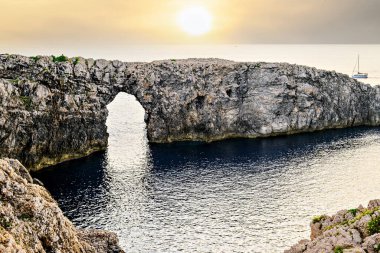 Ciutadella, Menorca, Balearic Adaları 'ndaki Pont den Gil Cala Corbetar' da muhteşem bir günbatımı. Kemer şeklinde tuhaf bir doğal oluşum.