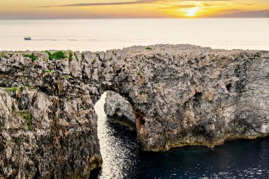 Ciutadella, Menorca, Balearic Adaları 'ndaki Pont den Gil Cala Corbetar' da muhteşem bir günbatımı. Kemer şeklinde tuhaf bir doğal oluşum.