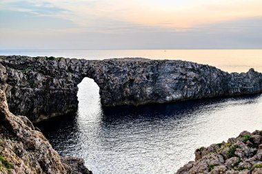 Ciutadella, Menorca, Balearic Adaları 'ndaki Pont den Gil Cala Corbetar' da muhteşem bir günbatımı. Kemer şeklinde tuhaf bir doğal oluşum.