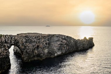 Ciutadella, Menorca, Balearic Adaları 'ndaki Pont den Gil Cala Corbetar' da muhteşem bir günbatımı. Kemer şeklinde tuhaf bir doğal oluşum.