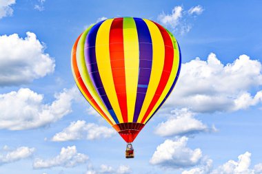 Colorful hot air balloon flying over blue sky with white clouds clipart