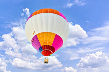 Mavi gökyüzünde beyaz bulutlarla uçan renkli sıcak hava balonu