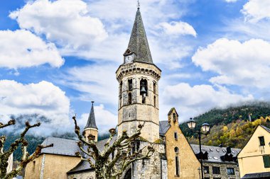 Church of San Miguel in Romanesque-Gothic style, in Viella, Valle de Aran, Catalonia, Spain, under a blue sky with white clouds clipart