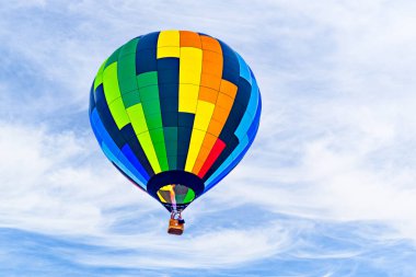 Mavi gökyüzünde beyaz bulutlarla uçan renkli sıcak hava balonu