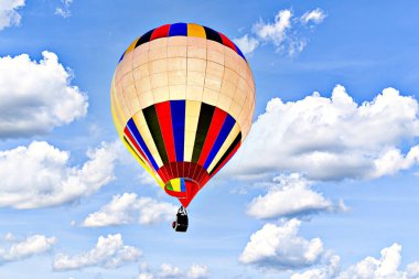 Mavi gökyüzünde beyaz bulutlarla uçan renkli sıcak hava balonu