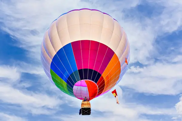 Mavi gökyüzünde beyaz bulutlarla uçan renkli sıcak hava balonu