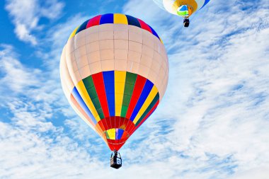 Mavi gökyüzünde beyaz bulutlarla uçan renkli sıcak hava balonu