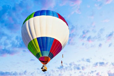 Mavi gökyüzünde beyaz bulutlarla uçan renkli sıcak hava balonu