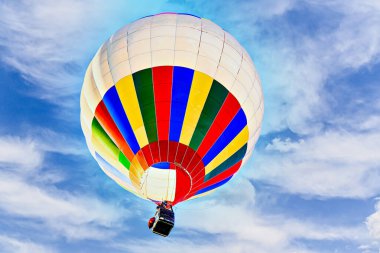 Mavi gökyüzünde beyaz bulutlarla uçan renkli sıcak hava balonu