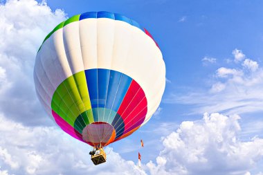 Mavi gökyüzünde beyaz bulutlarla uçan renkli sıcak hava balonu