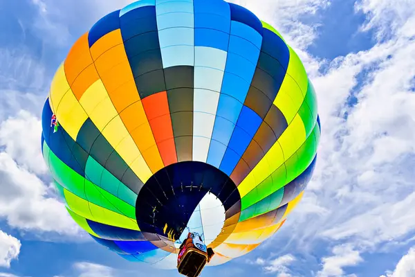 Mavi gökyüzünde beyaz bulutlarla uçan renkli sıcak hava balonu